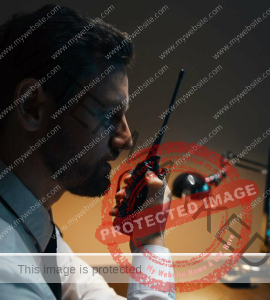 Portrait of a male security guard at the workplace. The guard is holding a walkie-talkie, he checks the security posts.